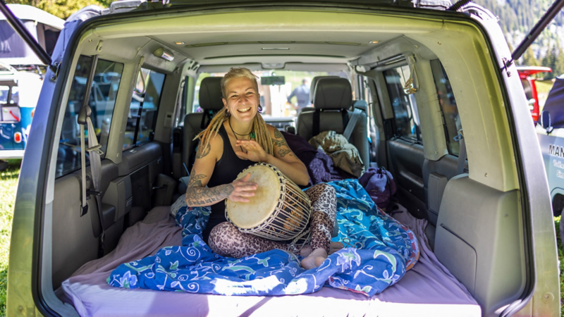 Noemi sitzt in ihrem VW Bus T4 und spielt Trommel.
