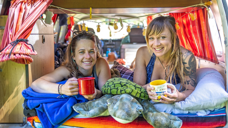 Zwei Frauen liegen in einem VW Bus T2a und halten Becher in der Hand.