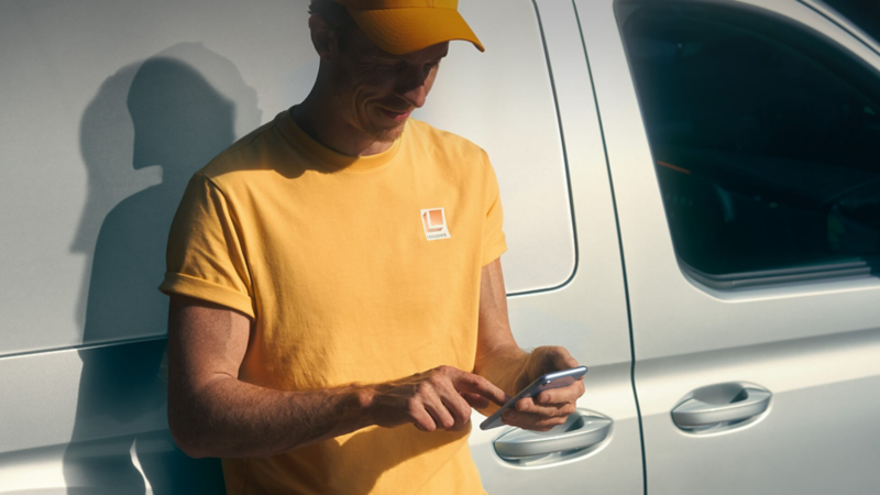 Photo showing a man standing next to a VW van using his phone. 