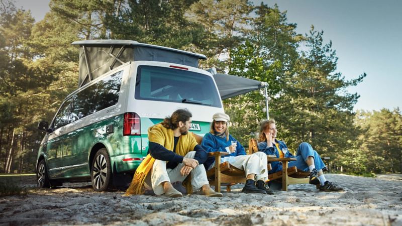 Three friends sitting next to California camper van on the beach