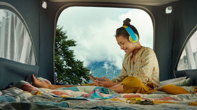 Photo of a girl listening to music through headphones in the back of a VW motorhome. 