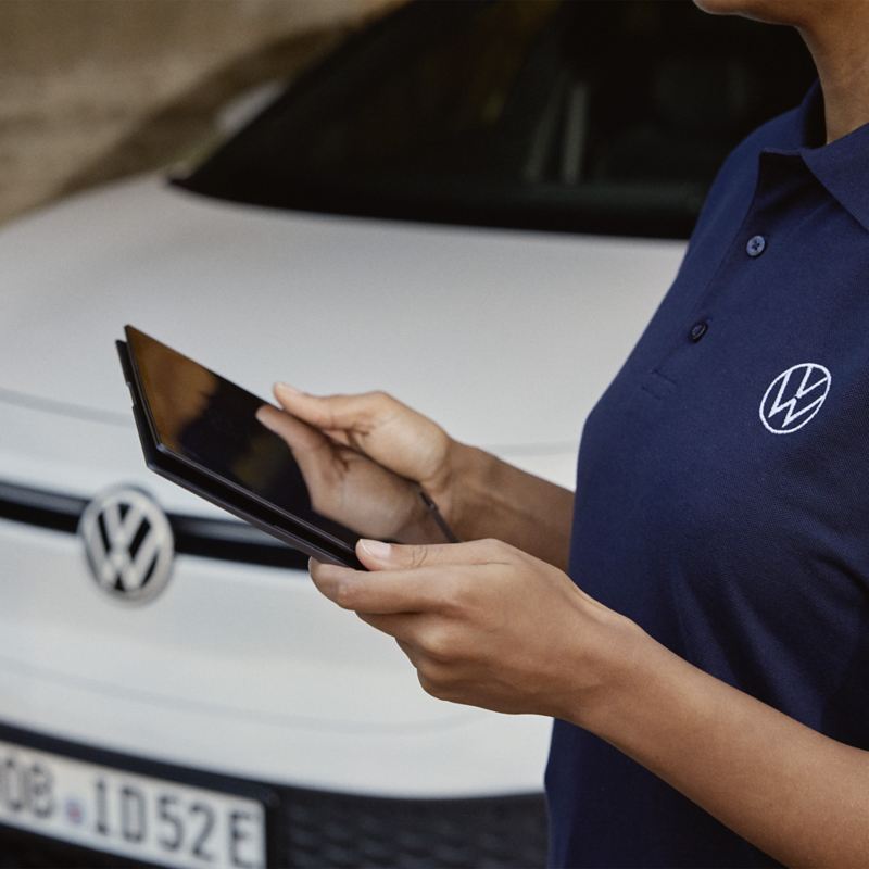Eine Person bedient ein Tablet. Im Hintergrund ein VW ID.5. – Angebote mit Versicherung