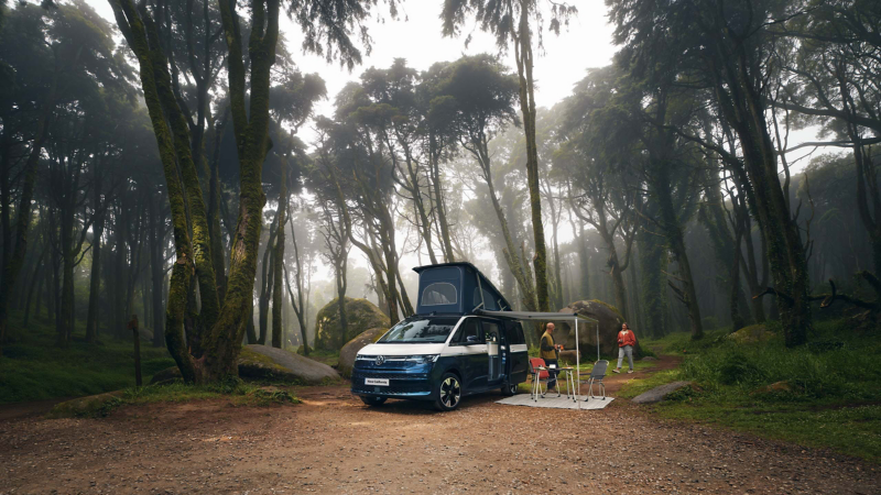 Photo of a California parked in a forest with the awning and dining accessories deployed.