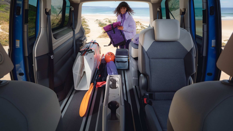 Photo of a California parked on a beach with two people sat in front of it eating.