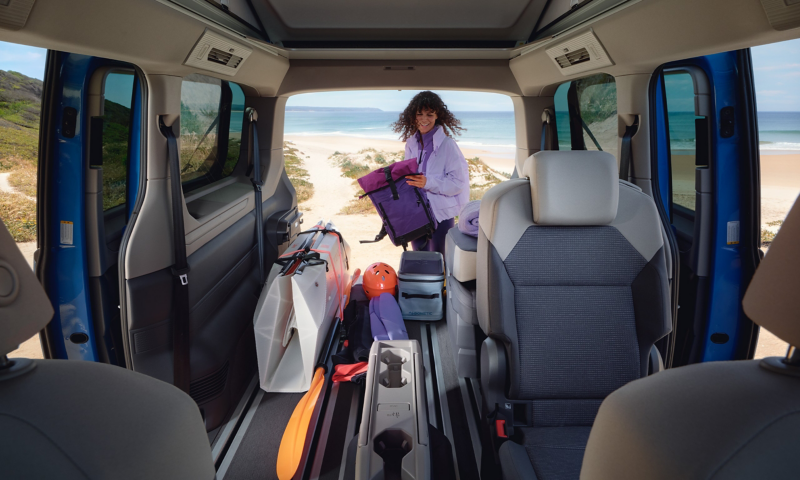 Het interieur van een VW California en een vrouw die inlaadt via de open achterklep.