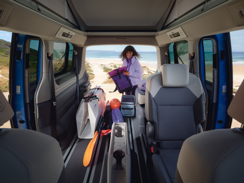 Das innere eines VW California, welcher an einem Strand steht und von einer Frau entladen wird.