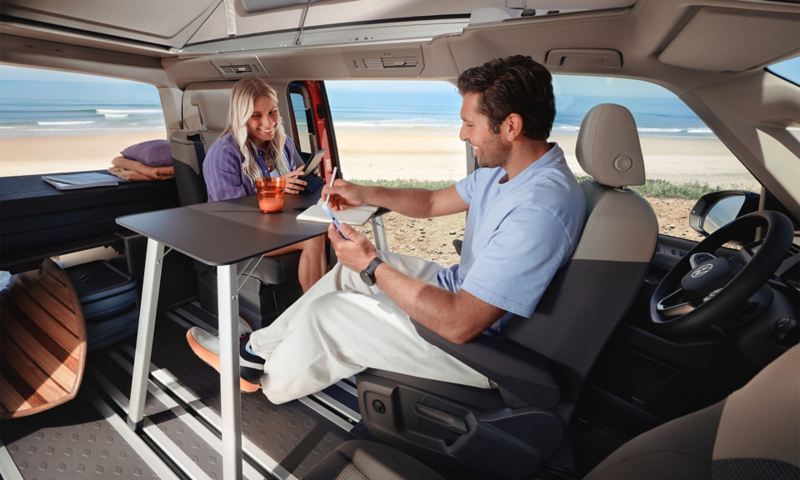 Un homme et une femme assis à la table pliante dans l’habitacle d’un Volkswagen California.