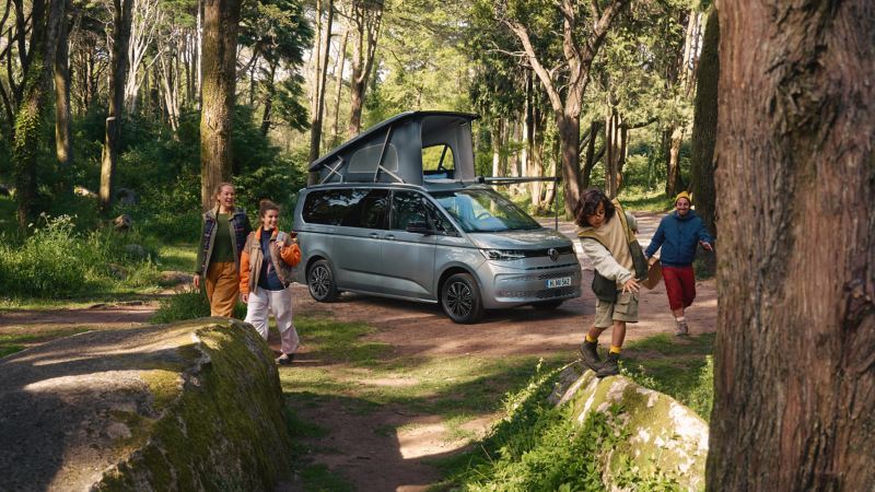 De VW California staat in het bos met het dak uitgeklapt.