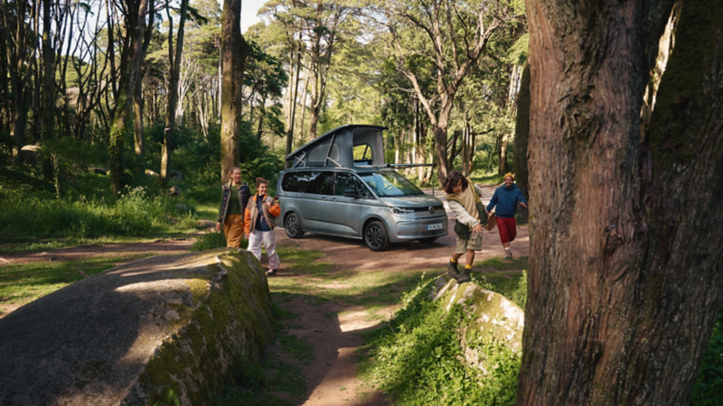 Eine Familie ist mit ihrem VW California COAST zum Campen im Wald. Sie sind gerade angekommen und erkunden die Gegend.