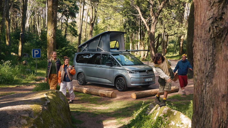 Une famille en camping dans la forêt avec leur VW California Coast. Ils viennent d'arriver et commencent à explorer les environs.