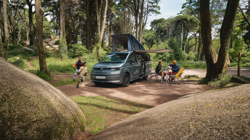 Photo showing a family sat outside, dining under the awning of their VW California.