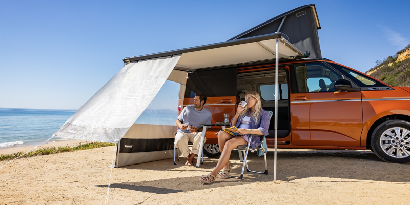 VW California mit aufgestellter Markise an einem Strand.