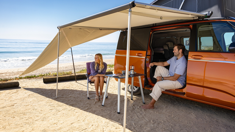 un homme et une femme assis dans le van california vw sur une plage