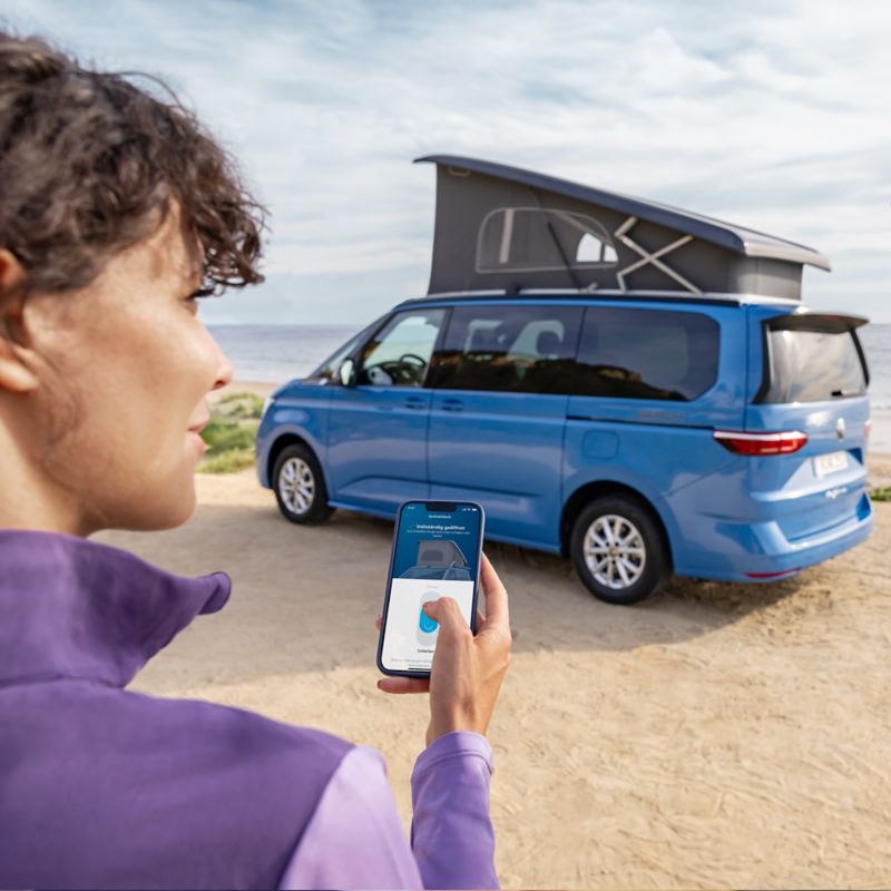 Photo of a California parked on a beach with a woman in front looking at the California app