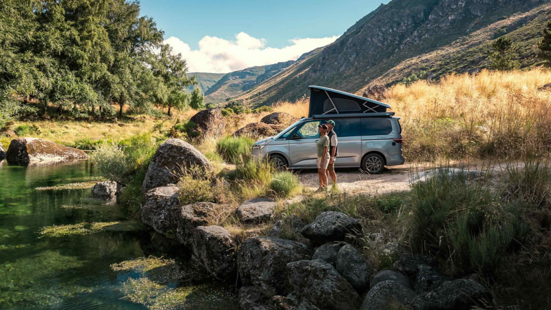 A VW California parked by a lake with two people standing next to it.