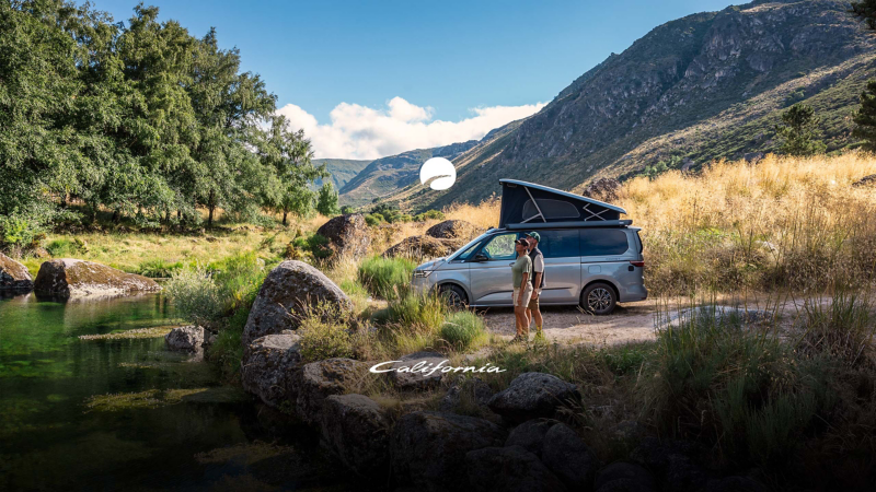 En VW California med uppfällt tak står parkerad vid en bäck.