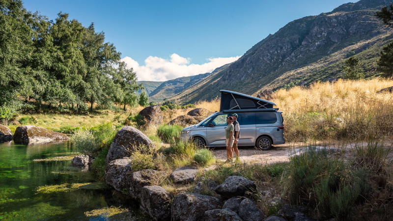 Ein Pärchen steht neben einem geparkten VW California und schauen auf einen See.