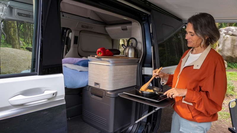 Ein Vater und sein Kind stehen an der Outdoor-Küche des VW California und kochen.