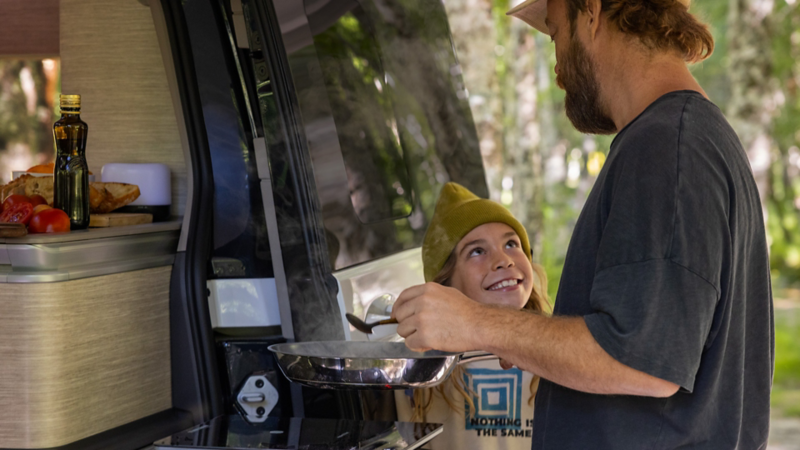 A father and his child stand cooking at the VW California’s outdoor kitchen.