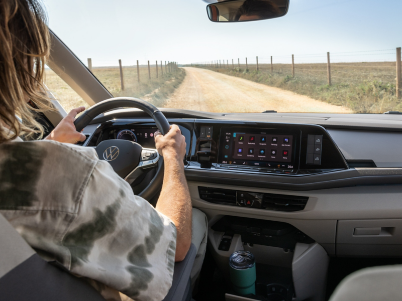 Eine Frau fährt in einem VW California einen Feldweg entlang.
