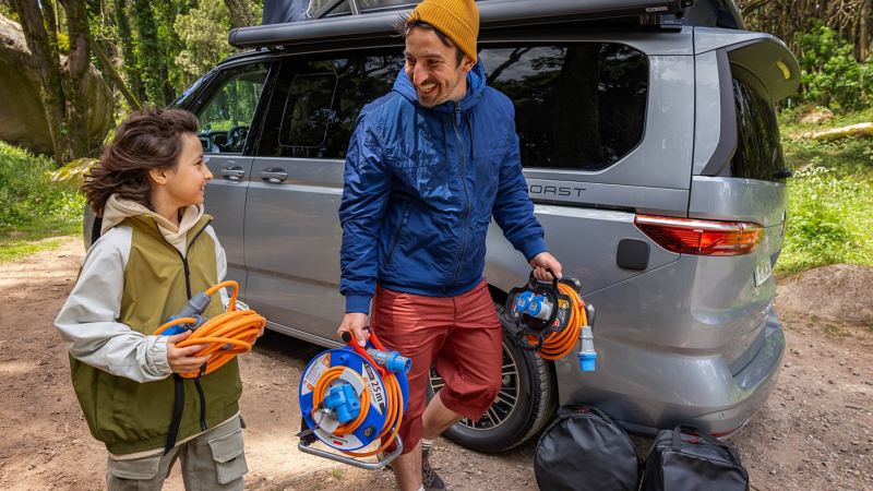 Ein Mann und ein Kind laufen mit Kabeln neben einem VW California.