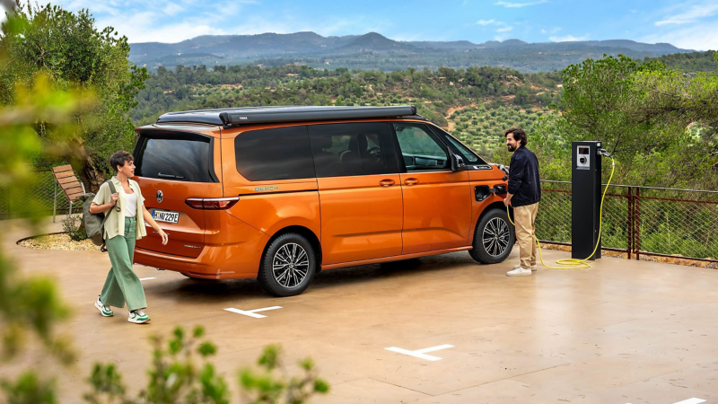 an orange California ehybrid being plugged into a changer on top of a hill overlooking mountains