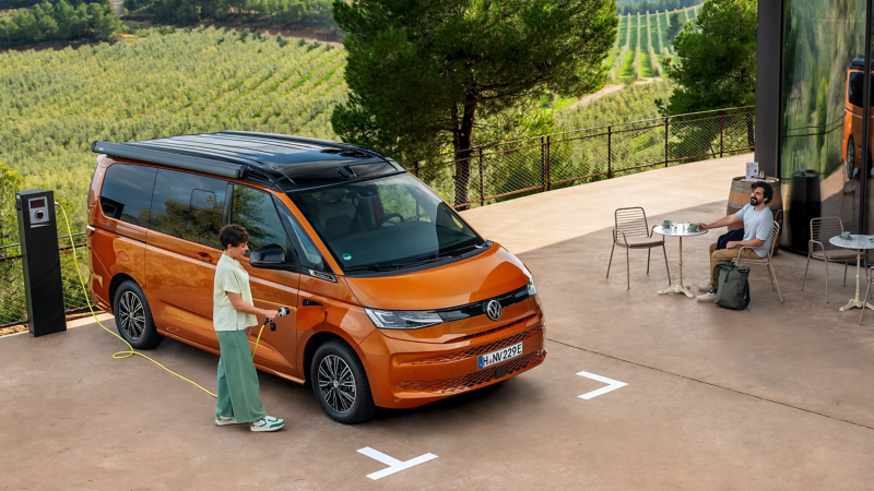Un VW California eHybrid orange est en cours de recharge sur une borne publique