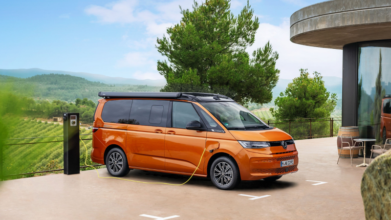 Ein VW California lädt an einer Ladestation neben einem Restaurant