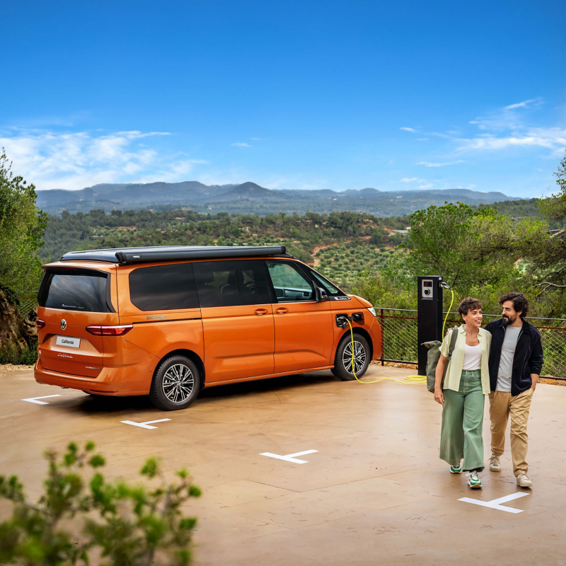 The new California parked on a beach with the roof unit opened and 2 people standing closeby