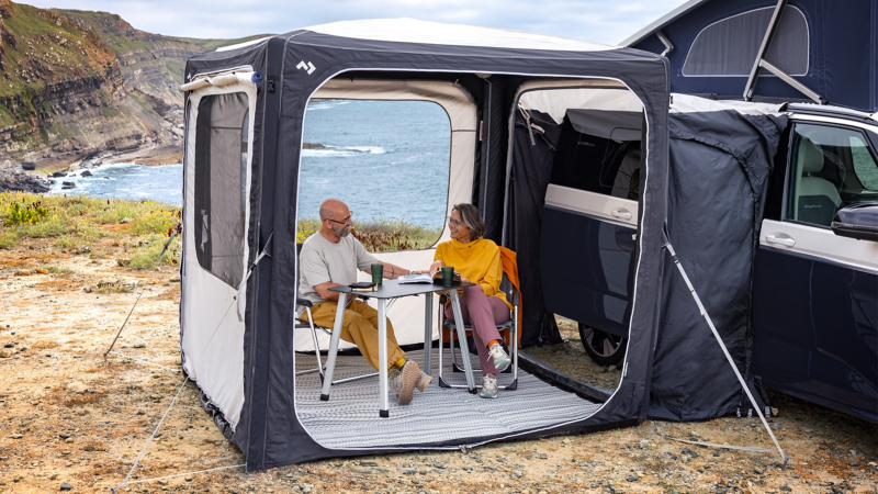 Ein Mann und eine Frau sitzen im aufgebauten Vorzelt Ihres VW California.