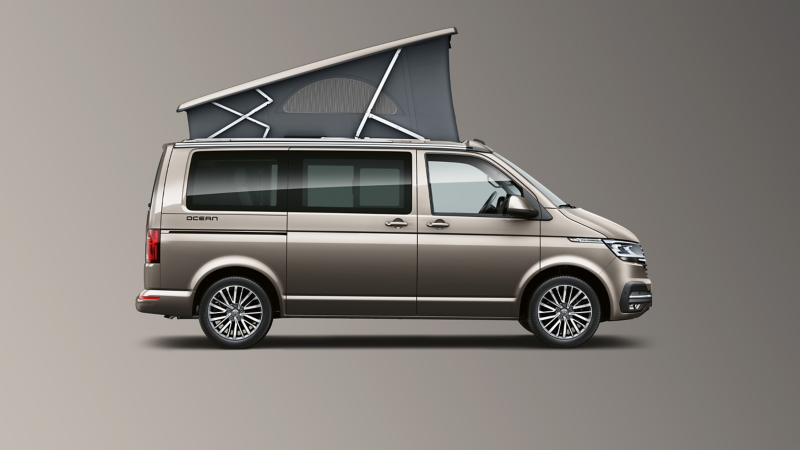 Un van Volkswagen California 6.1, avec un toit relevable gris, est présenté de profil sur un fond uni gris.
