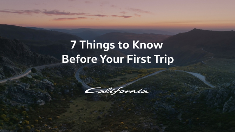 A VW California drives leisurely down a road through a picturesque mountain landscape