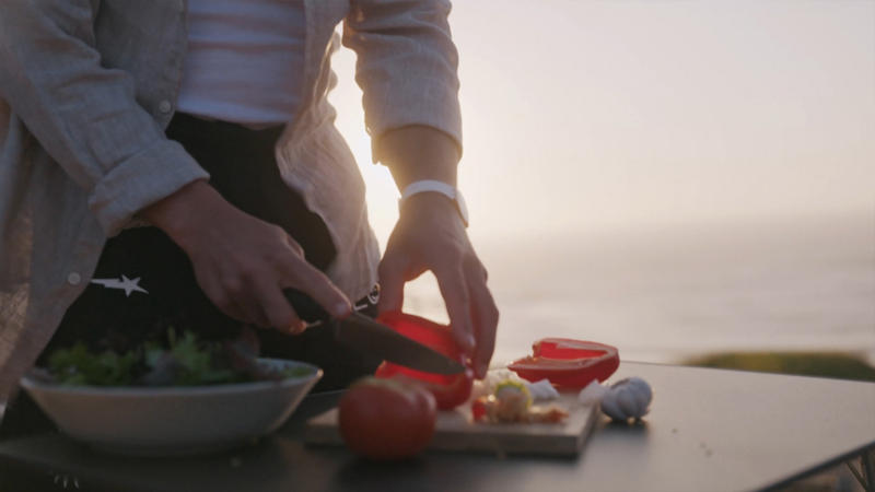 Eine Person schneidet im Licht des Sonnenuntergangs frisches Gemüse für einen Salat.