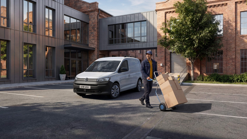 a man wheeling a large box walking away from a new VW Caddy Cargo