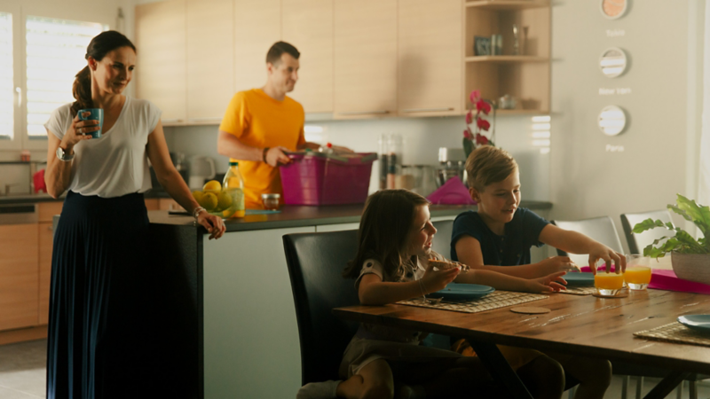 Zwei Kinder sind am Frühstücken, während die Eltern sich für den Alltag vorbereiten