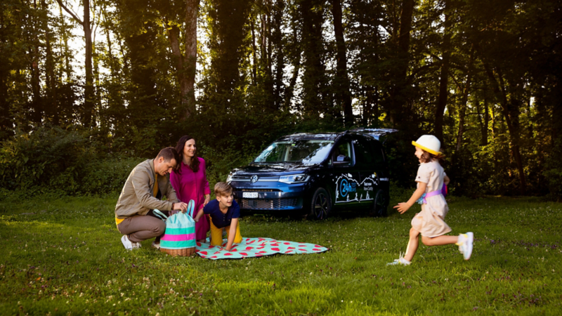 Eine Familie ist am Picknicken und ein Mädchen rennt zu der Familie