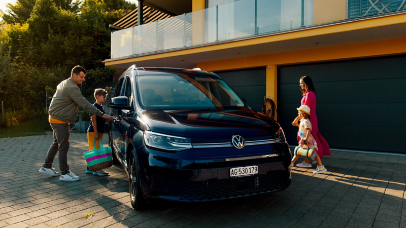 Eine Familie steig in den Caddy, der von vorne links ersichtlich ist, ein