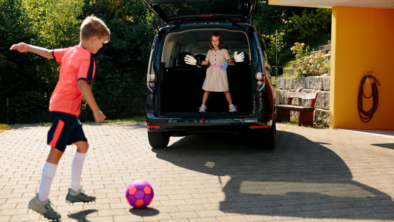 Zwei Kinder spielen Fussball und benutzen den Kofferraum vom Caddy als Tor