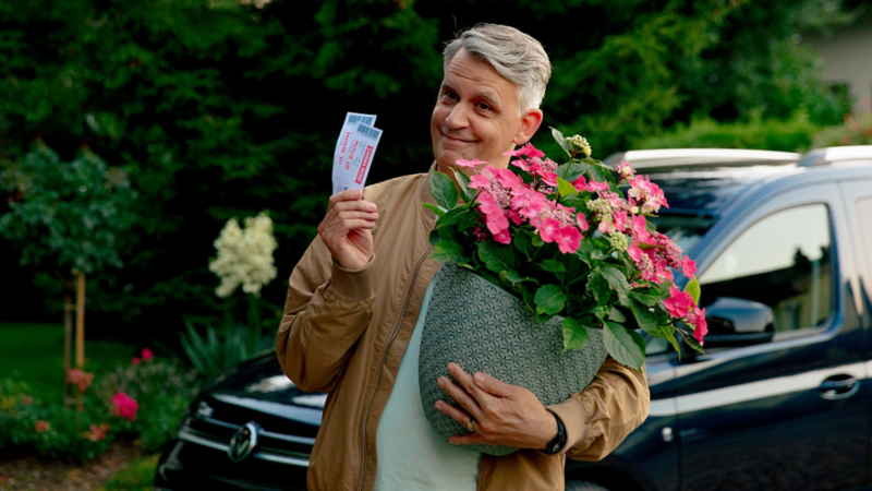 Ein Mann hält in einer Hand einen Blumentopf und in der anderen zwei Tickets
