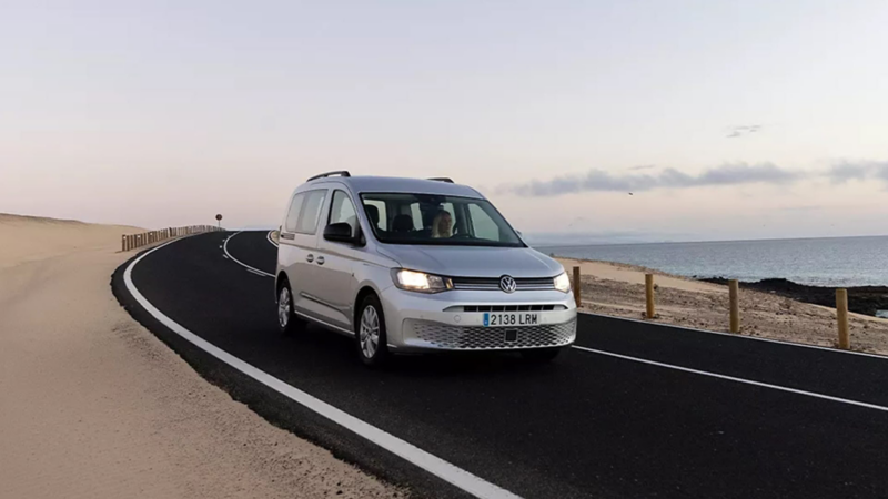 Una Caddy de ocasión gris metalizada al atardecer por un camino de carretera natural con el mar al fondo
