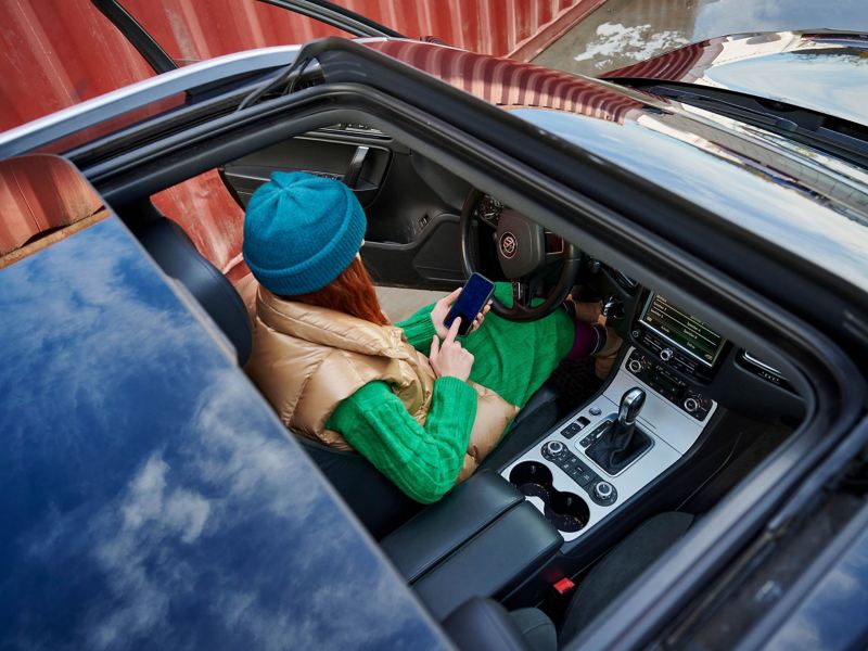 A woman sitting in a convertible car and holding her mobile phone