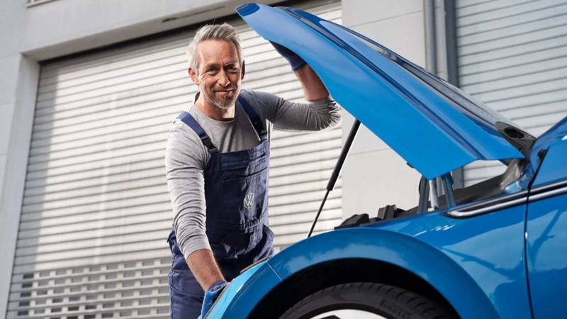Técnico de Volkswagen revisa el motor de un auto de color azul. 