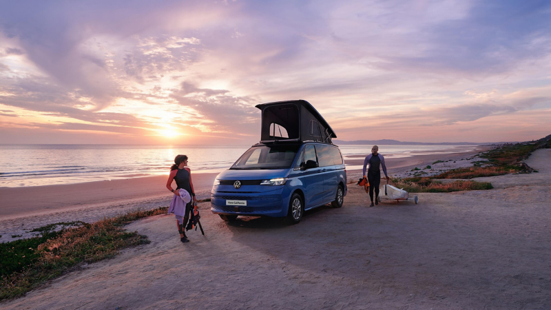 The new California parked on a beach with the roof unit opened and 2 people standing closeby