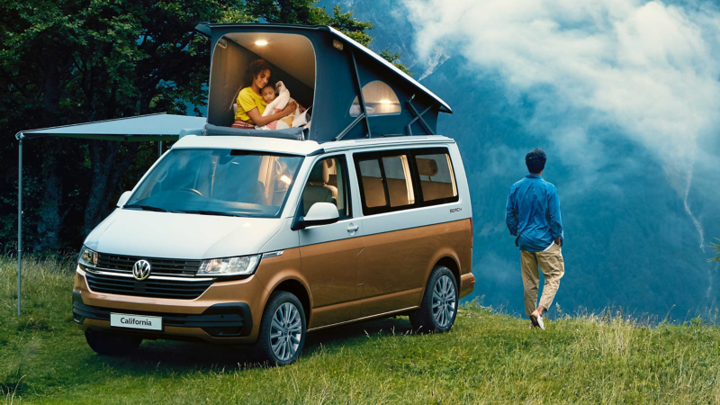 Man overlooking a valley with family in rooftop tent of California Van