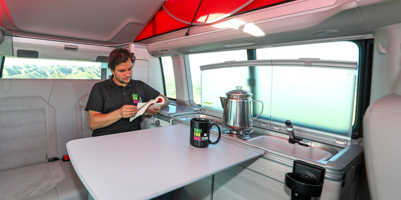 En mand sidder ved bordet i en Volkswagen California. På bordet står en kaffekop.
