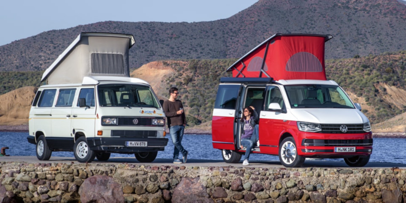 Zwei Volkswagen Nutzfahrzeuge California mit Hochdach stehen auf einer Mole am Meer.