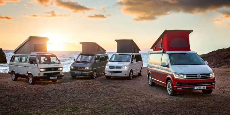 Vier Volkswagen Nutzfahrzeuge California unterschiedlicher Generationen stehen bei Sonnenuntergang am Strand.