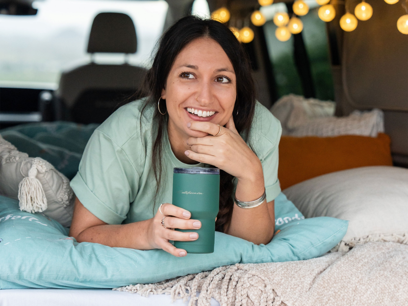 Eine Frau liegt im Bett mit einem Thermobecher aus der California Kollektion.