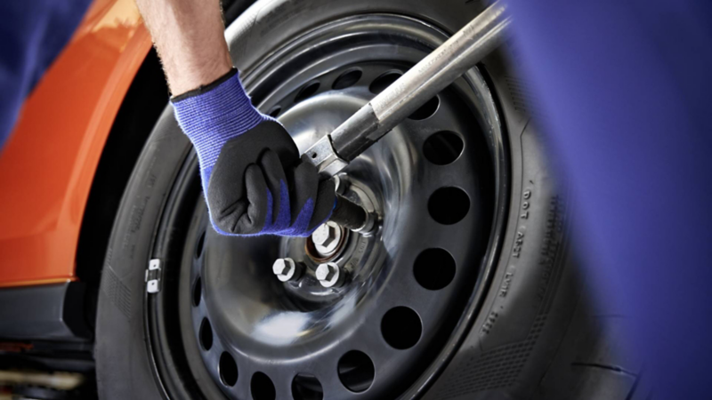 Técnico de Volkswagen aprieta tornillos del rin de una llanta con una llave cruz. 