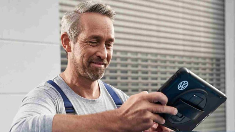 Técnico de Volkswagen revisa tableta digital donde apunta elementos a revisar de auto. 